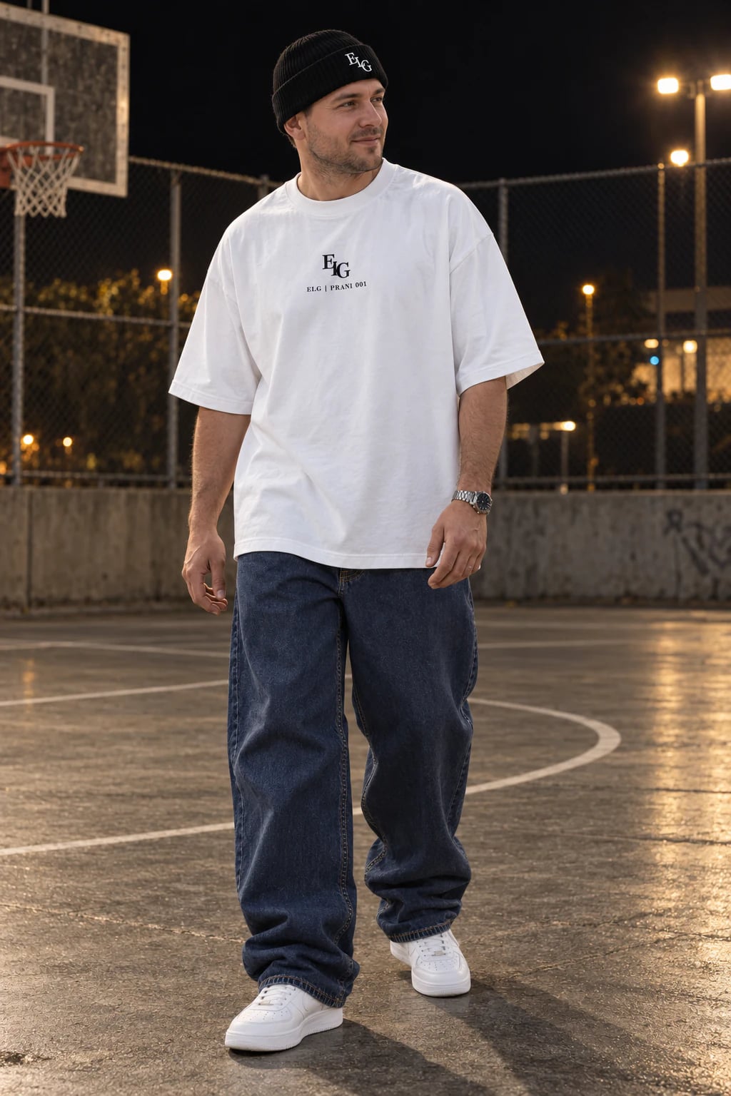 KI-Kampagnenbild eines jungen erwachsenen Mannes beim natürlichen Gehen neben einem Betonplatz bei Nacht, mit weißem ELG-T-Shirt über dem Hosenbund, schwarzer Beanie und tief indigoblauen Baggy-Jeans über schlichten weißen Sneakern.