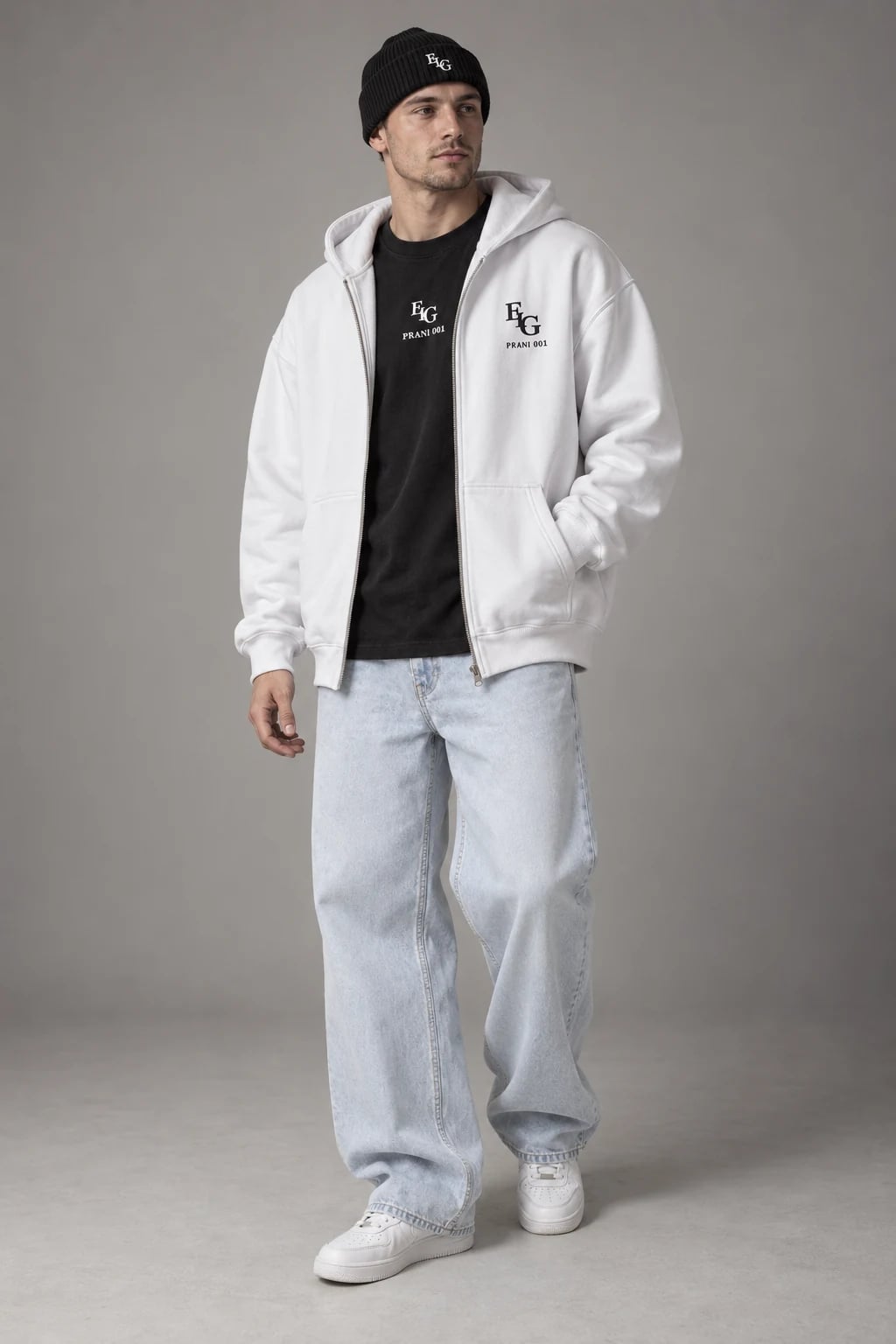 Pamje me AI: burrë i ri i rritur në këmbë në studio me tone neutrale, me hoodie ELG të bardhë, bluzë të zezë jashtë pantallonave, kapelë të zezë dhe xhinse baggy blu shumë të zbehtë.